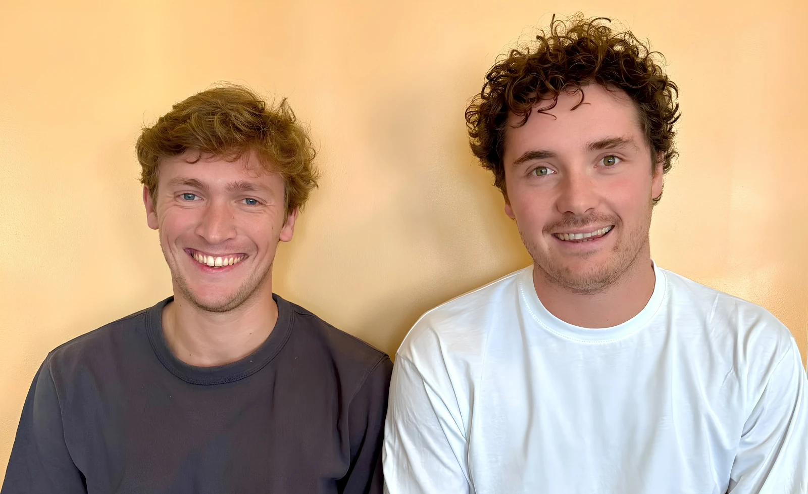 Photographie. Les deux associés de Vauban, côte à côte devant un mur ocre, souriants, en t-shirt.